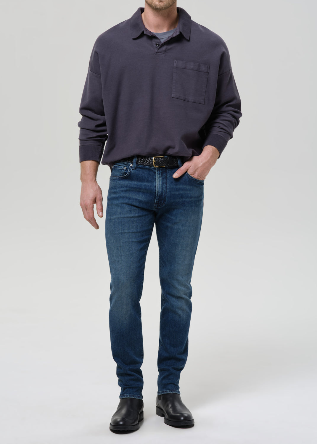 Man wearing a dark gray long-sleeve shirt and blue jeans on a grey background
