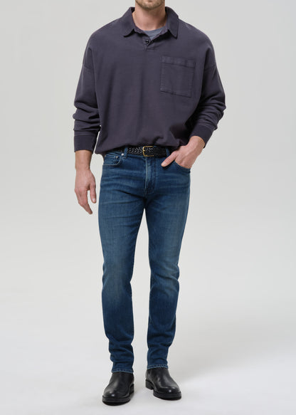 Man wearing a dark gray long-sleeve shirt and blue jeans on a grey background