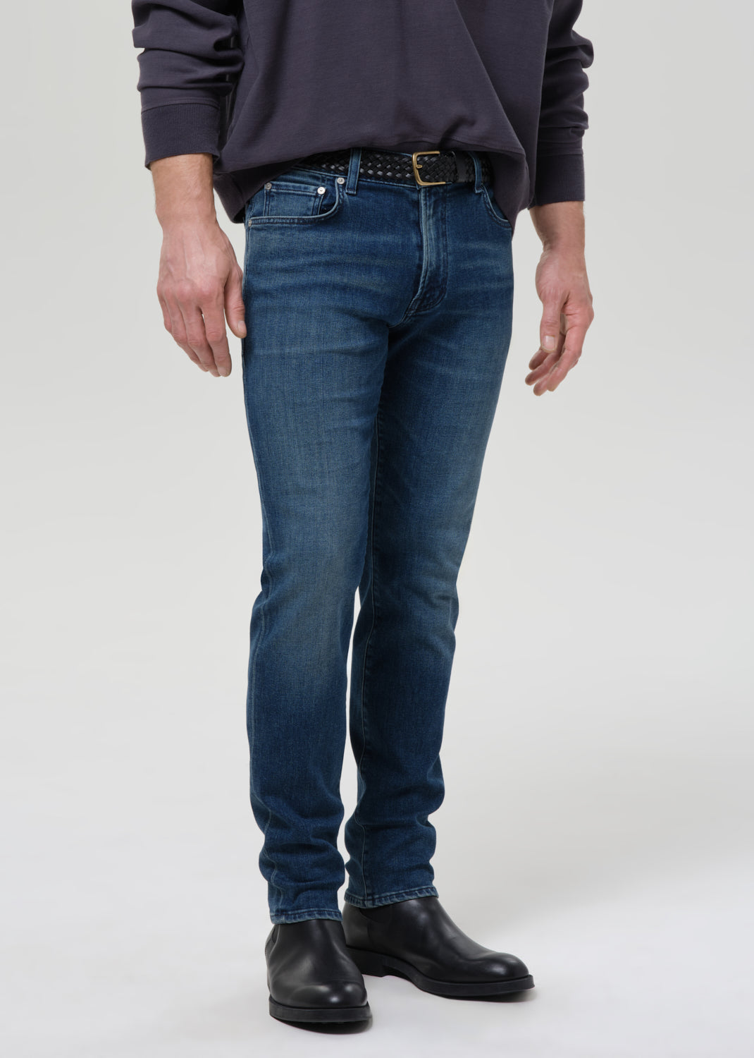 Person wearing blue jeans and black shoes on a grey background