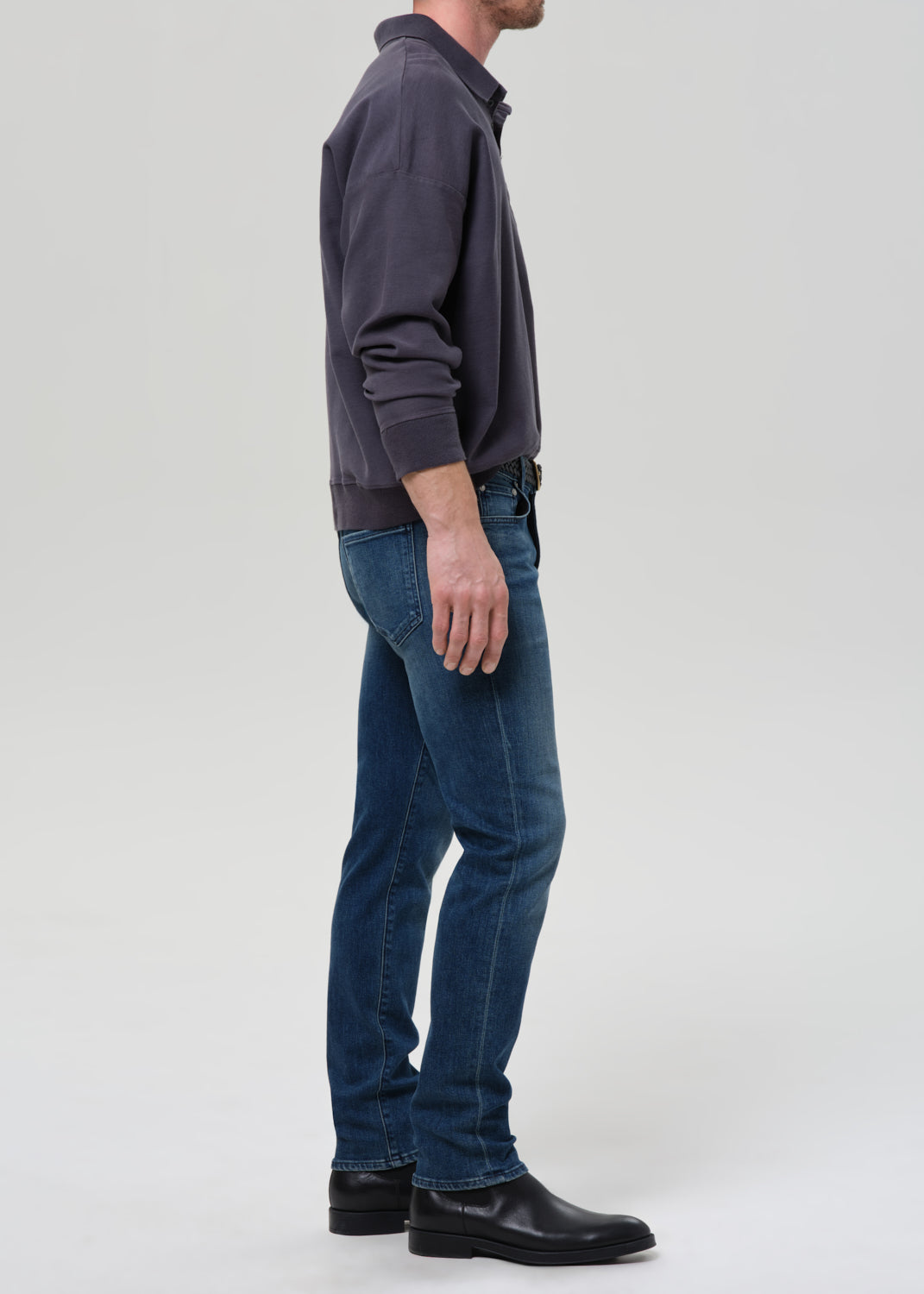 Person wearing a dark gray sweater and blue jeans on a grey background