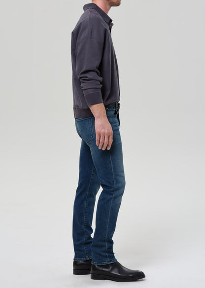 Person wearing a dark gray sweater and blue jeans on a grey background