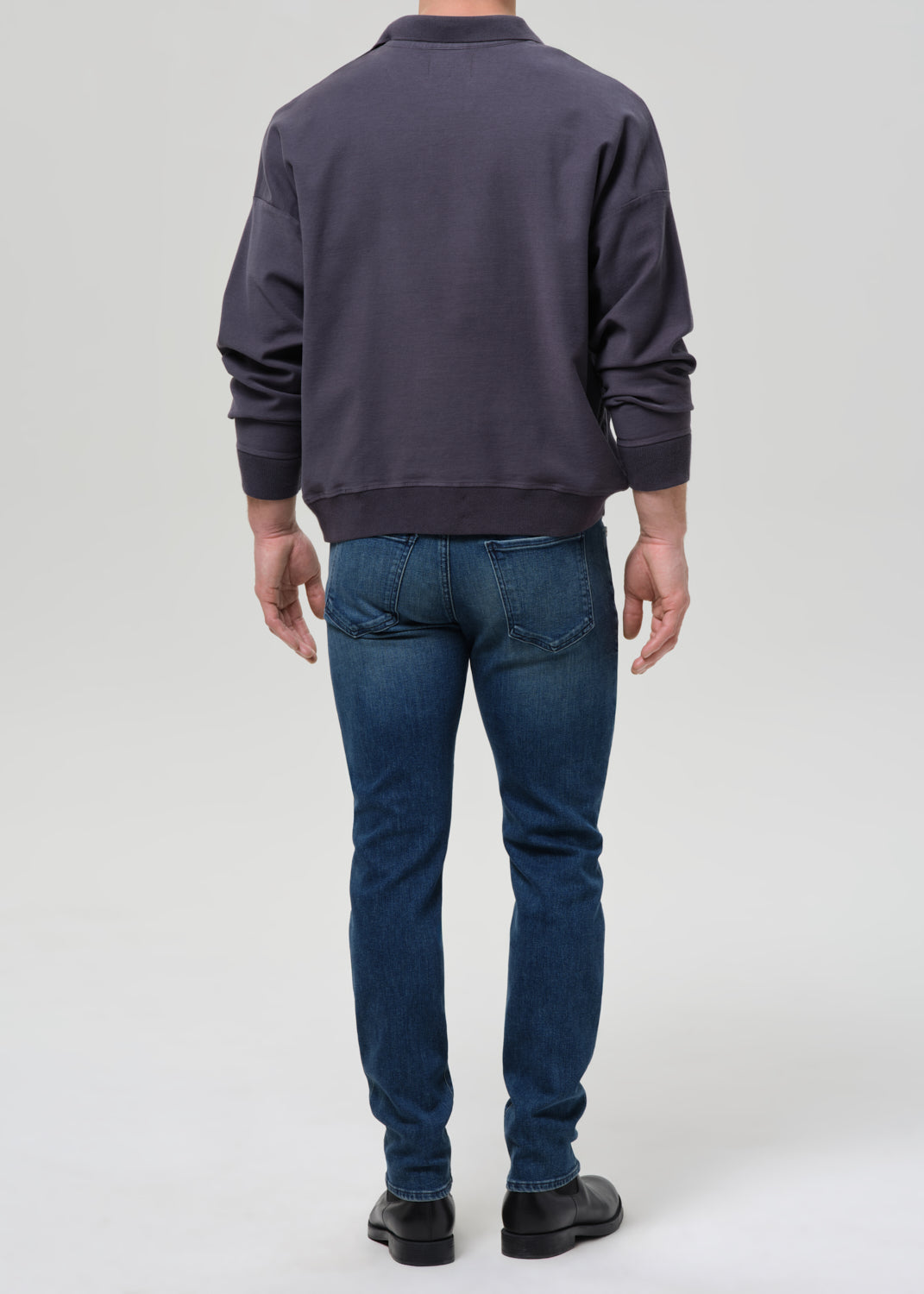 Person wearing a dark gray sweatshirt and blue jeans on a grey background