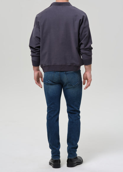 Person wearing a dark gray sweatshirt and blue jeans on a grey background