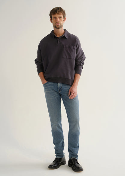 Person wearing medium blue straight leg jeans with a dark navy long sleeve collared pullover and black shoes, front full body view on a light grey background.
