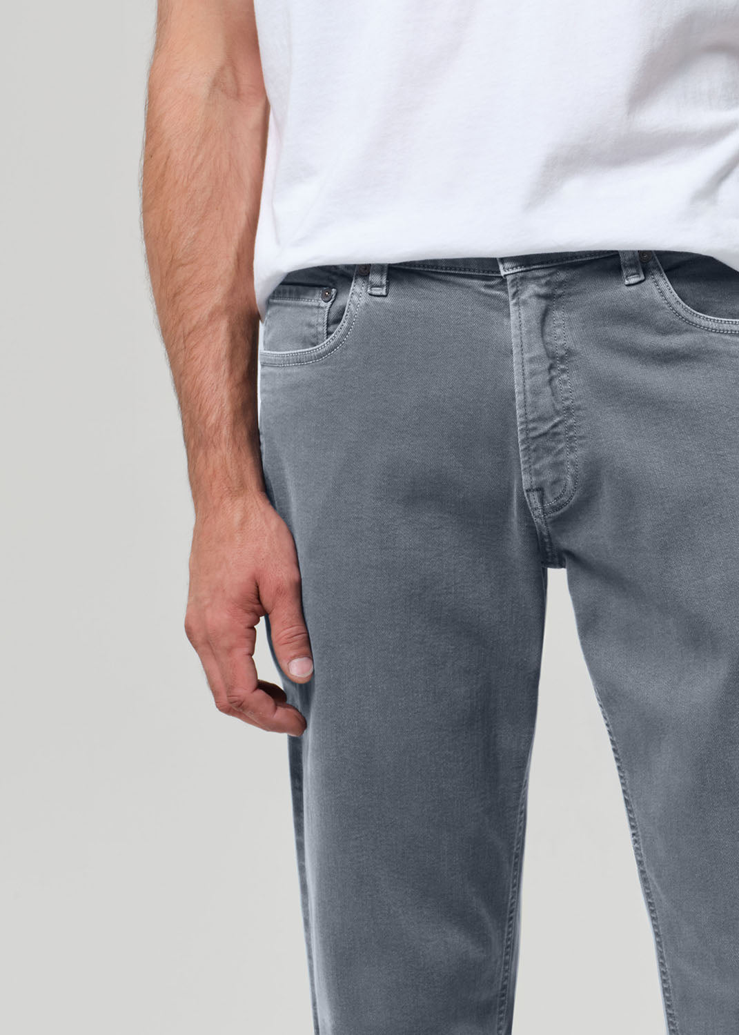 Person wearing gray jeans and a white shirt on a plain background