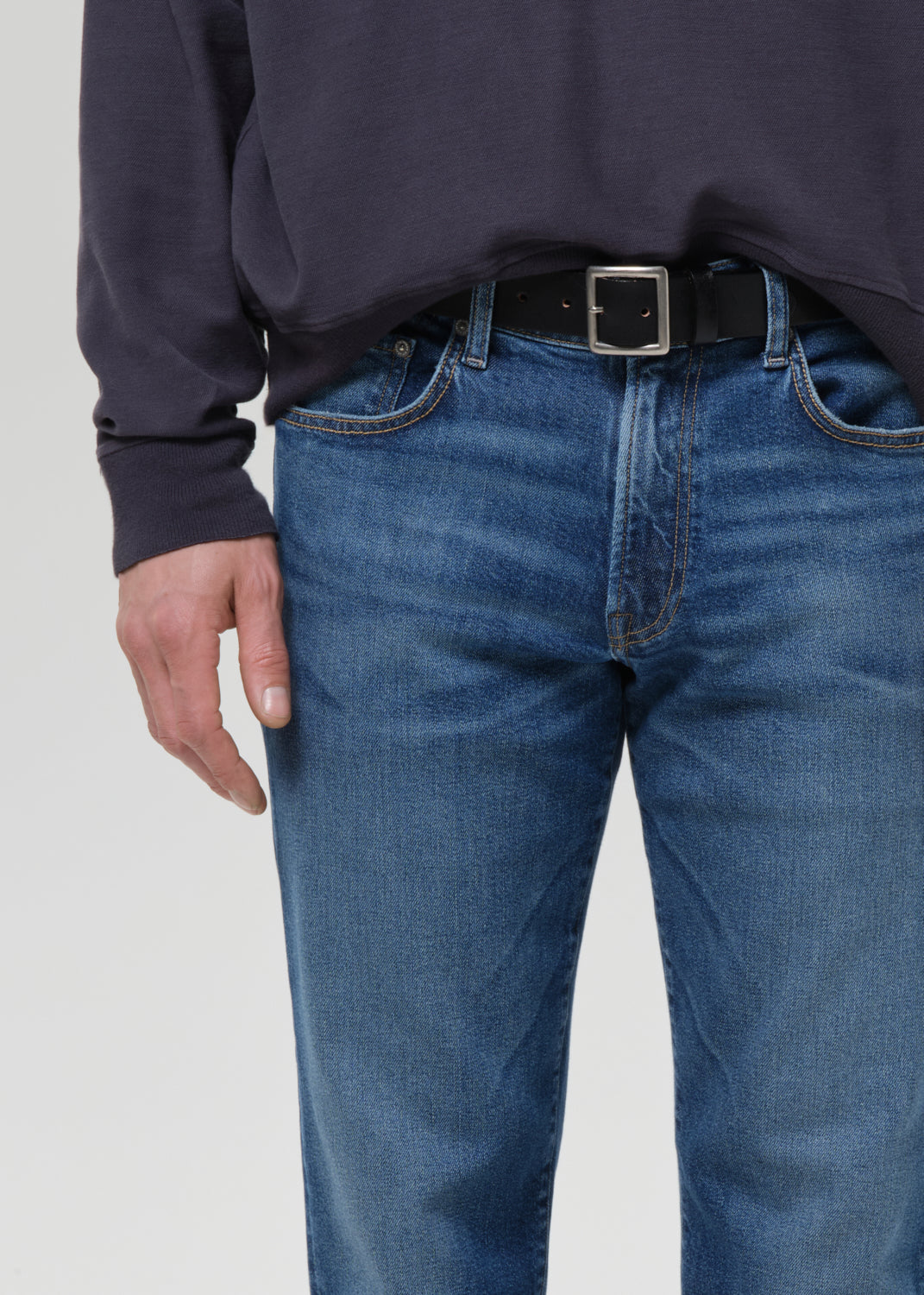 Person wearing blue jeans and a dark sweater on a grey background
