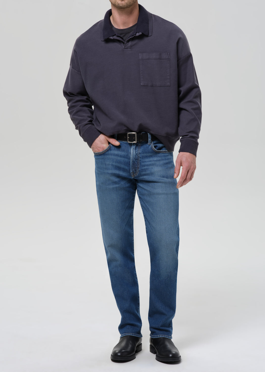 Person wearing a dark blue sweatshirt and jeans on a grey background