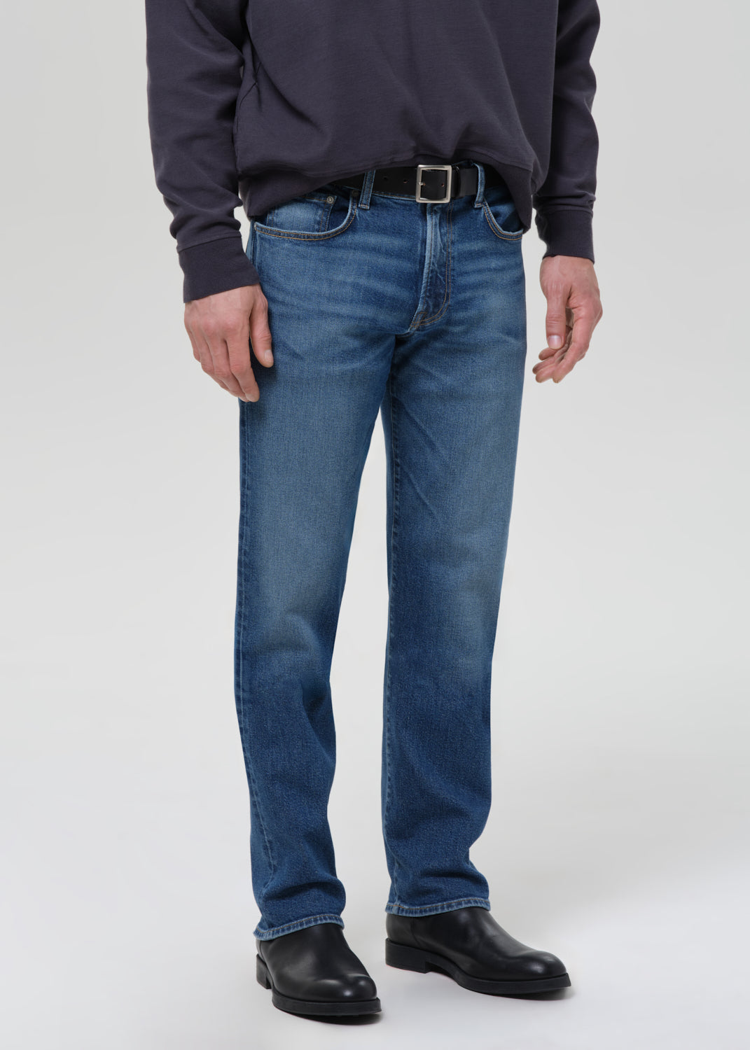 Person wearing blue jeans and a dark shirt on a grey background