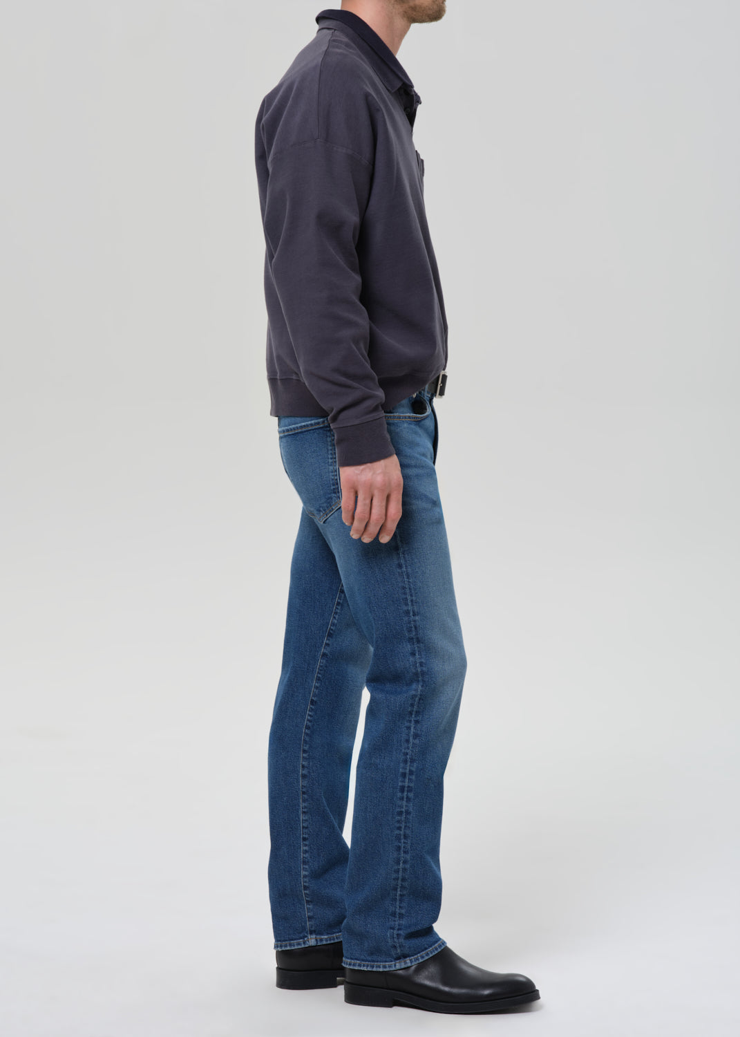 Person wearing a dark jacket and blue jeans on a grey background
