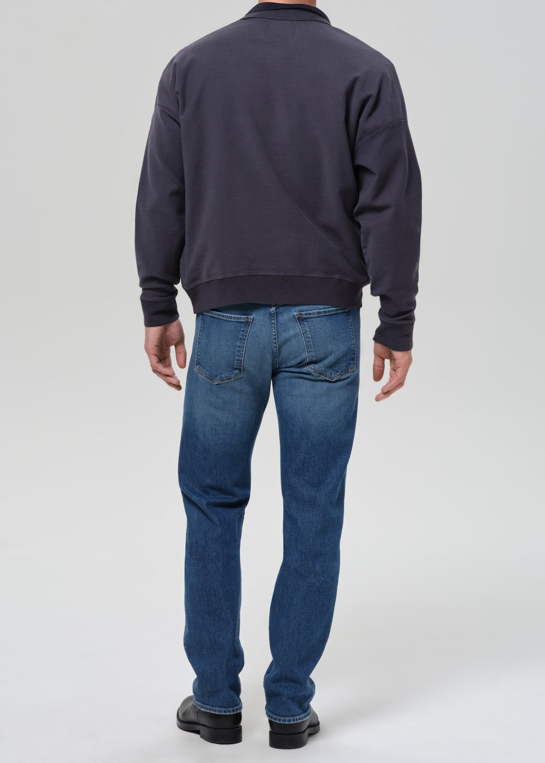 Person wearing a dark jacket and blue jeans on a grey background