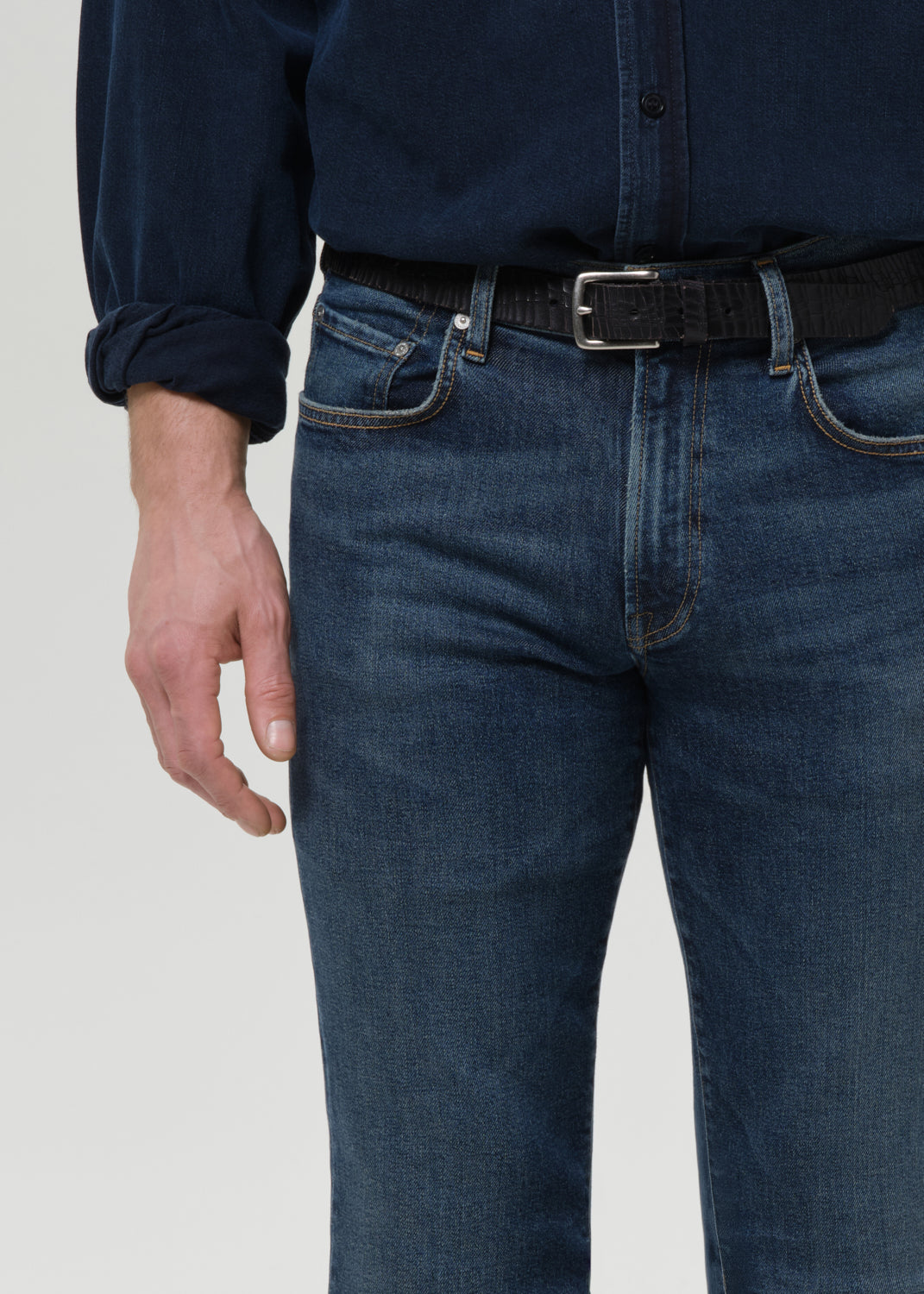 Person wearing a navy shirt and blue jeans with a black belt on a grey background