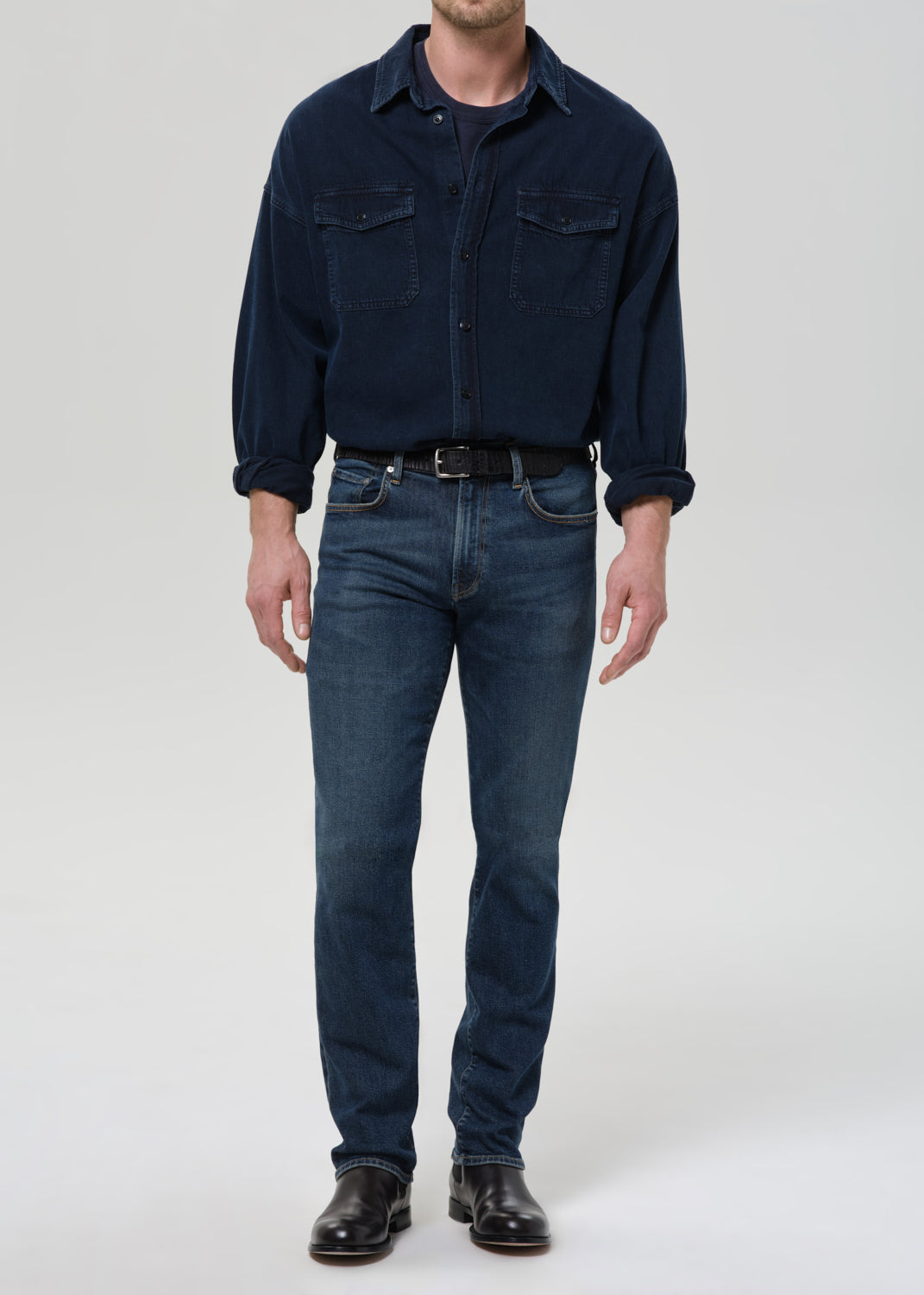 Person wearing a navy blue shirt and jeans on a grey background