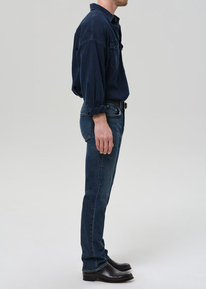Person wearing a dark blue shirt and jeans on a grey background