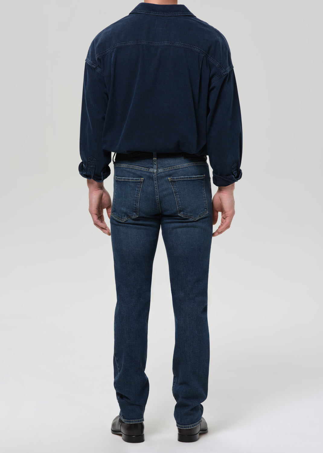 Person wearing a navy blue shirt and jeans on a grey background