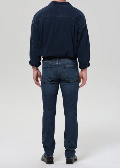 Person wearing a navy blue shirt and jeans on a grey background