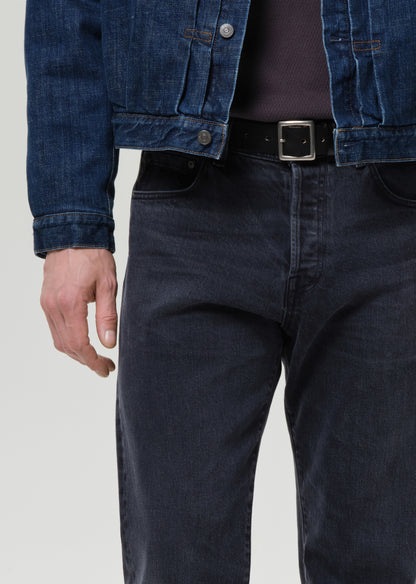Person wearing a blue denim jacket and dark jeans on a grey background