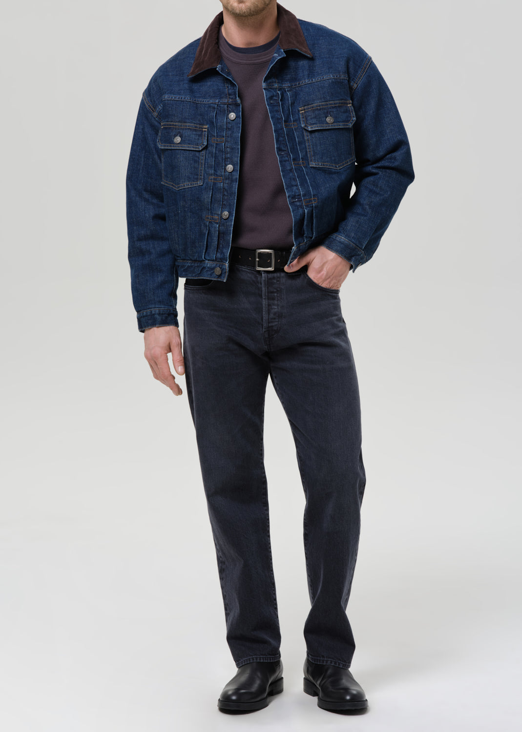 Person wearing a blue denim jacket and jeans on a grey background