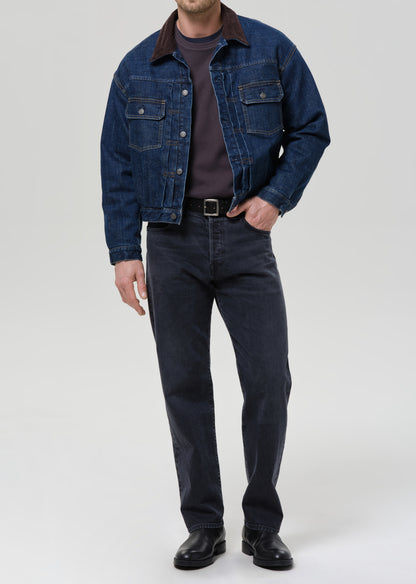 Person wearing a blue denim jacket and jeans on a grey background