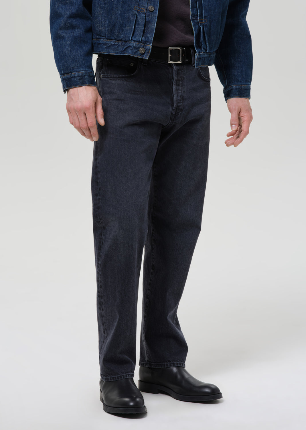 Person wearing dark jeans and a denim jacket on a grey background