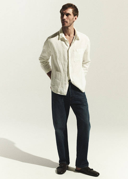 Man wearing a white shirt and dark jeans against a plain background