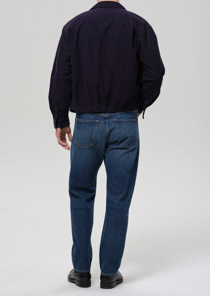 Back view of a person wearing a dark navy jacket and blue jeans against a grey background.