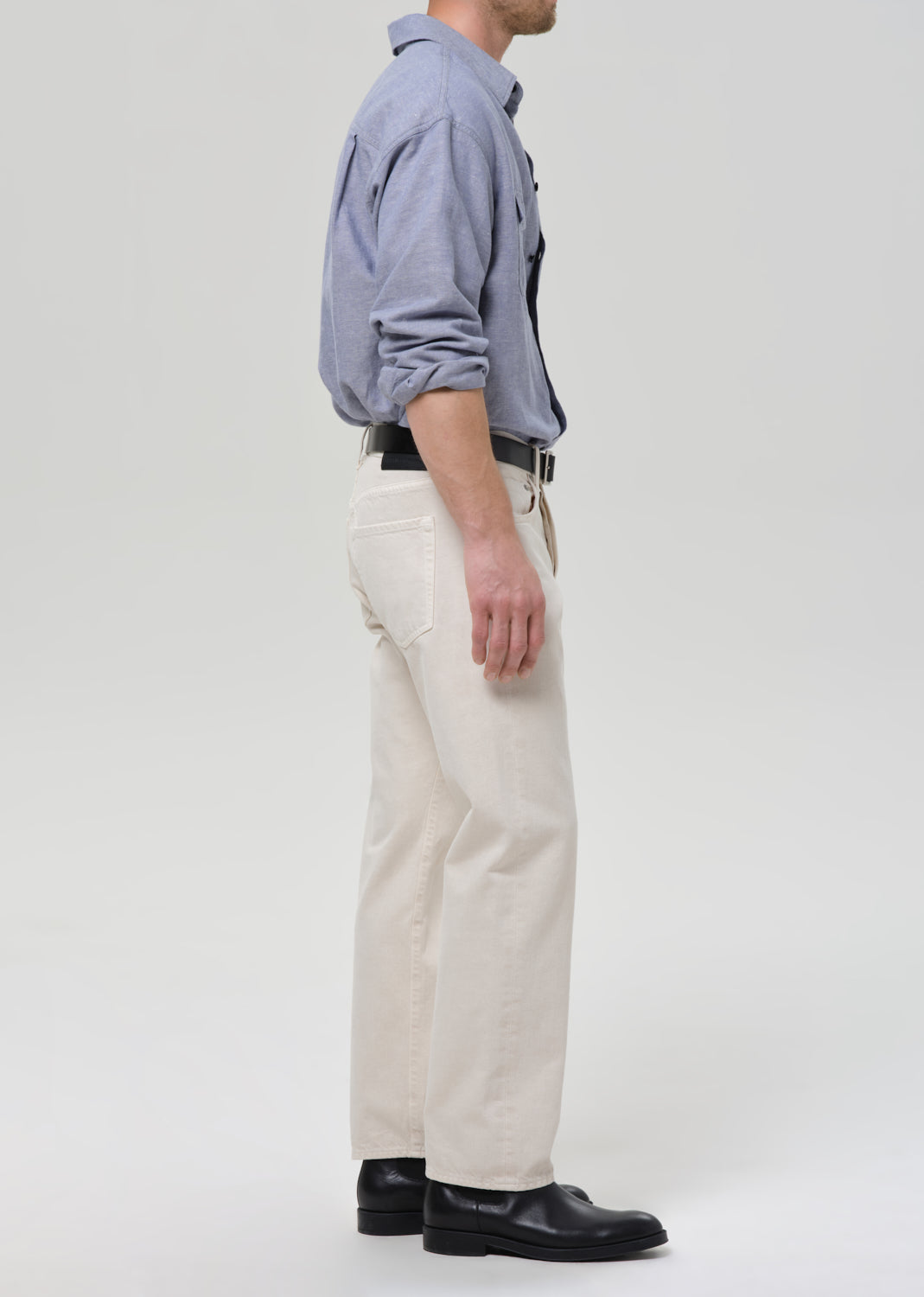 Person wearing a blue shirt, white pants, and black shoes on a grey background