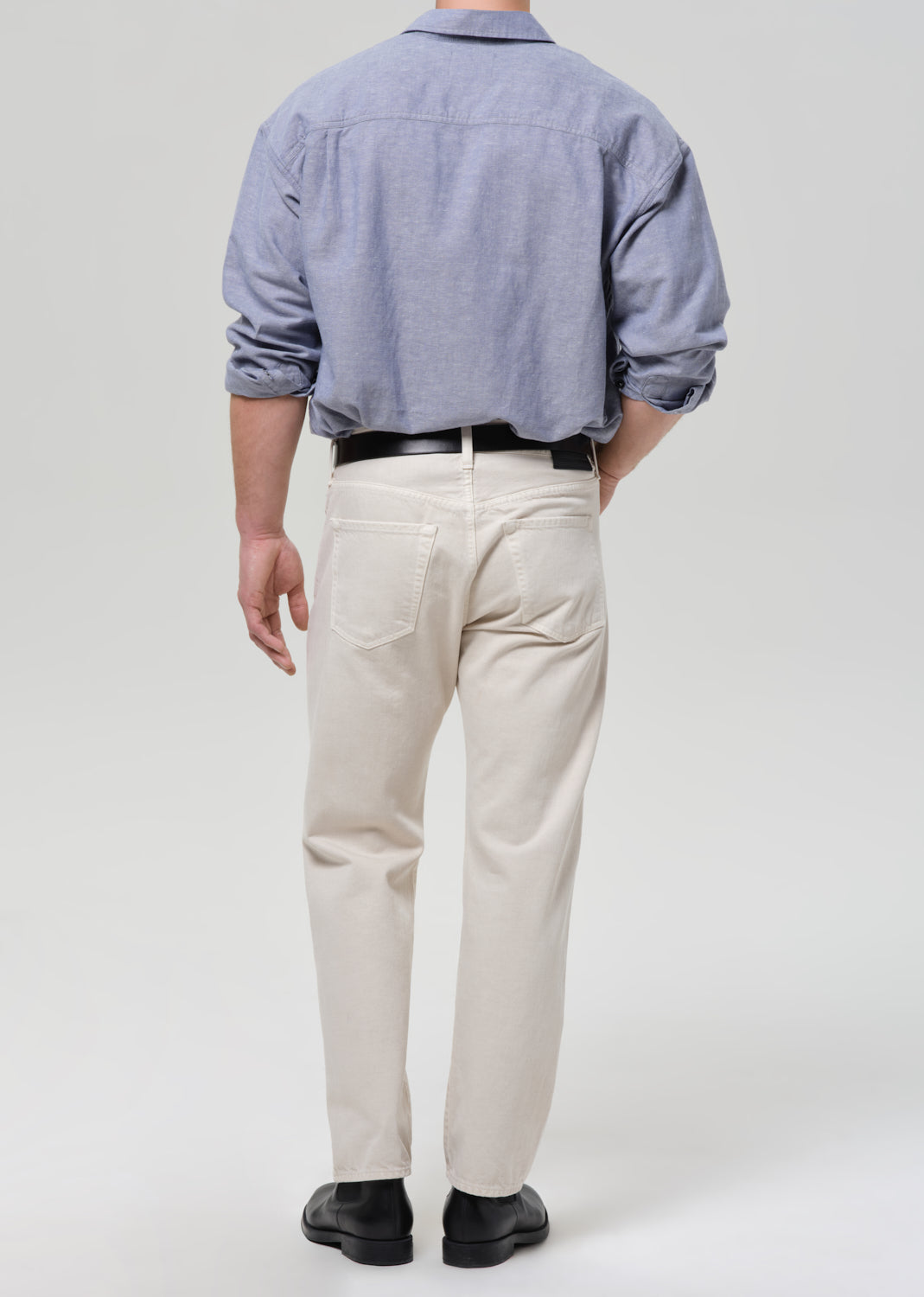Person wearing a blue shirt and beige pants on a grey background