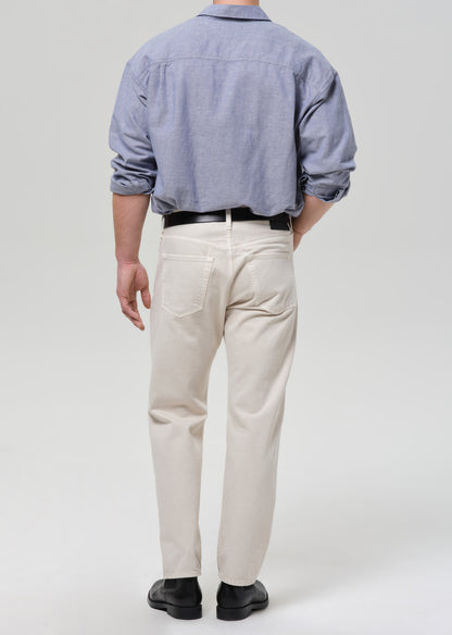 Person wearing a blue shirt and beige pants on a grey background