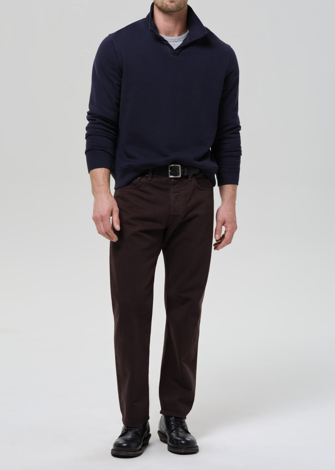 Man wearing a navy sweater, brown pants, and black shoes on a grey background