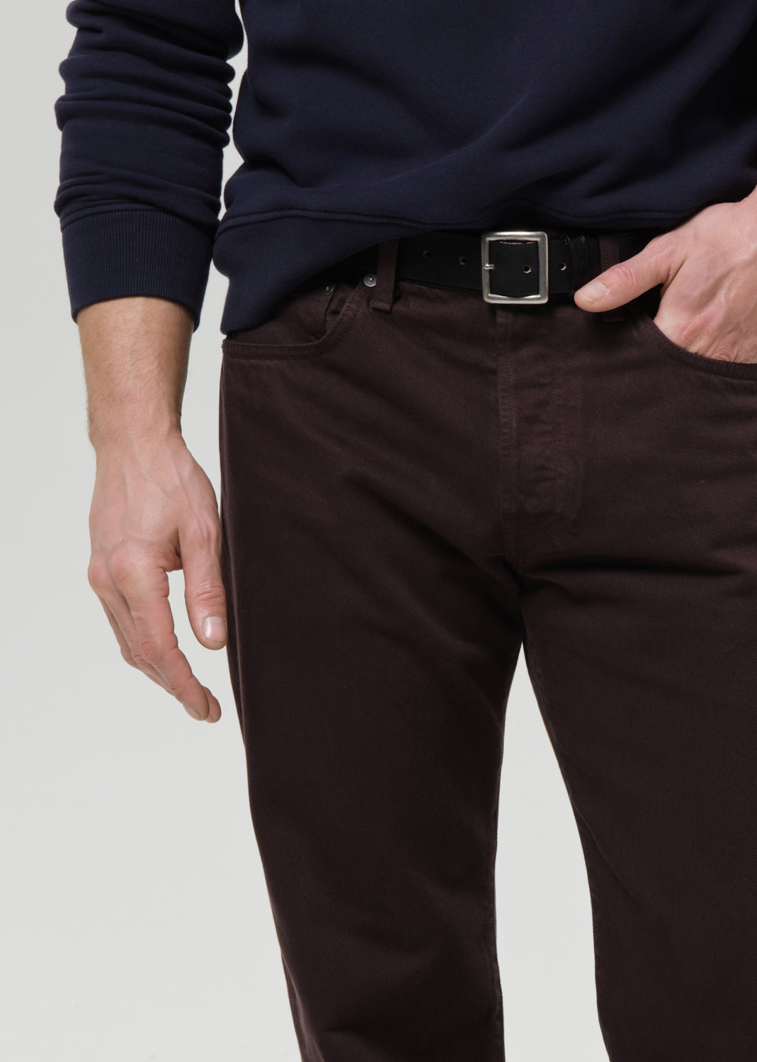 Person wearing a navy sweater and dark pants with a belt on a grey background
