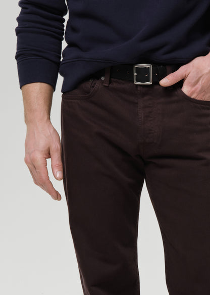 Person wearing a navy sweater and dark pants with a belt on a grey background