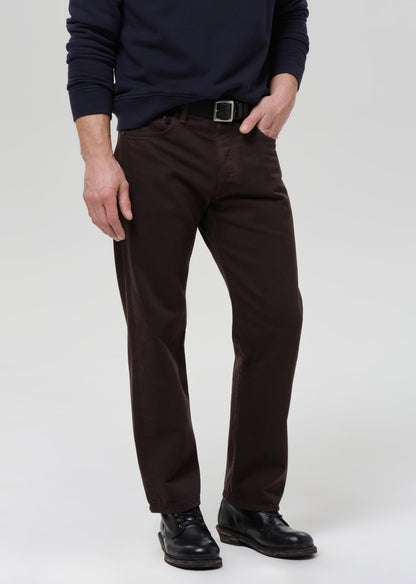 Person wearing dark brown pants and black shoes on a grey background