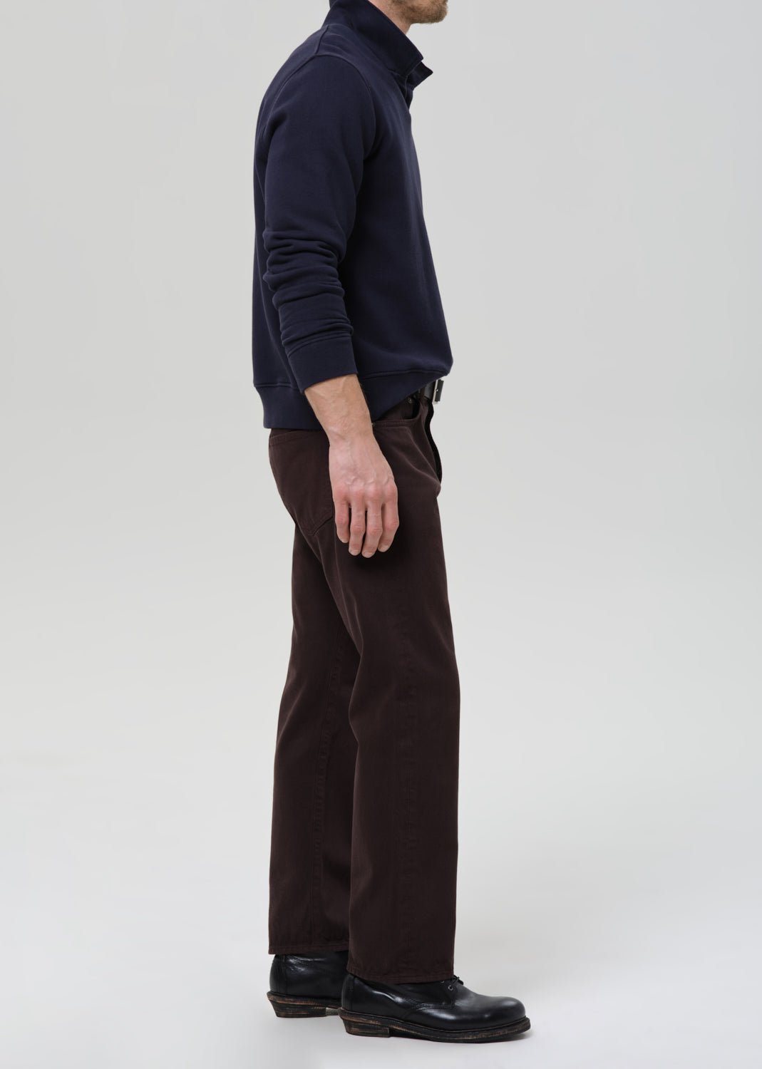 Person wearing a navy sweater and brown pants on a grey background