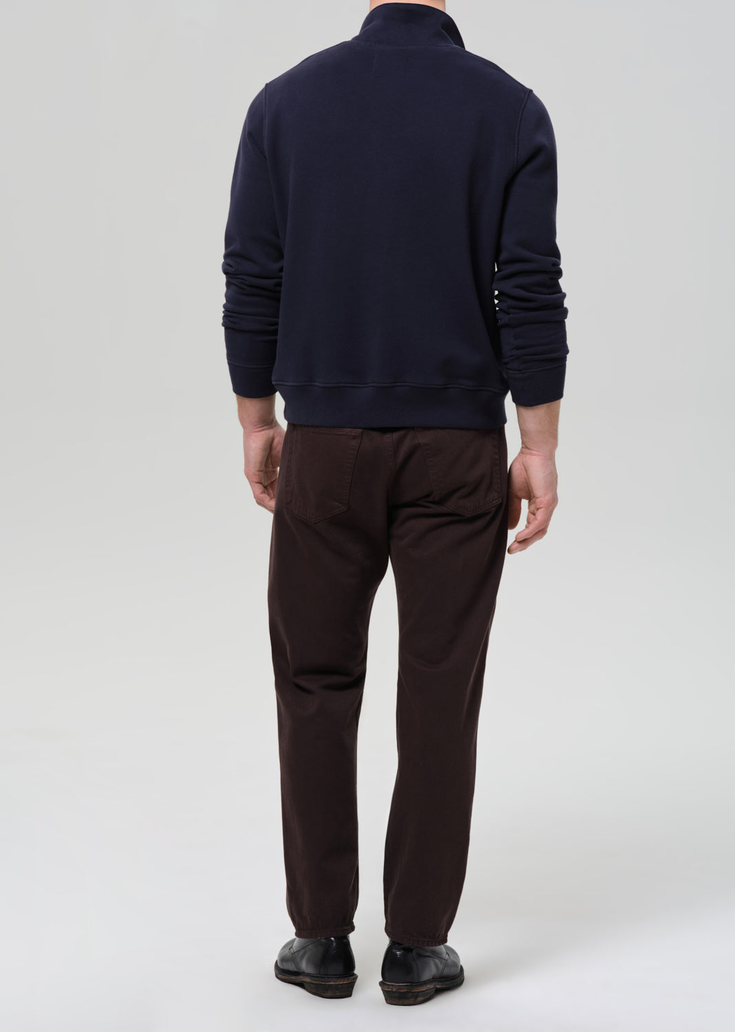 Person wearing a navy sweater and brown pants on a grey background