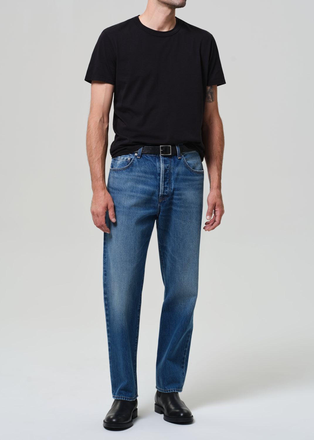 Person wearing a black t-shirt and blue jeans on a plain background