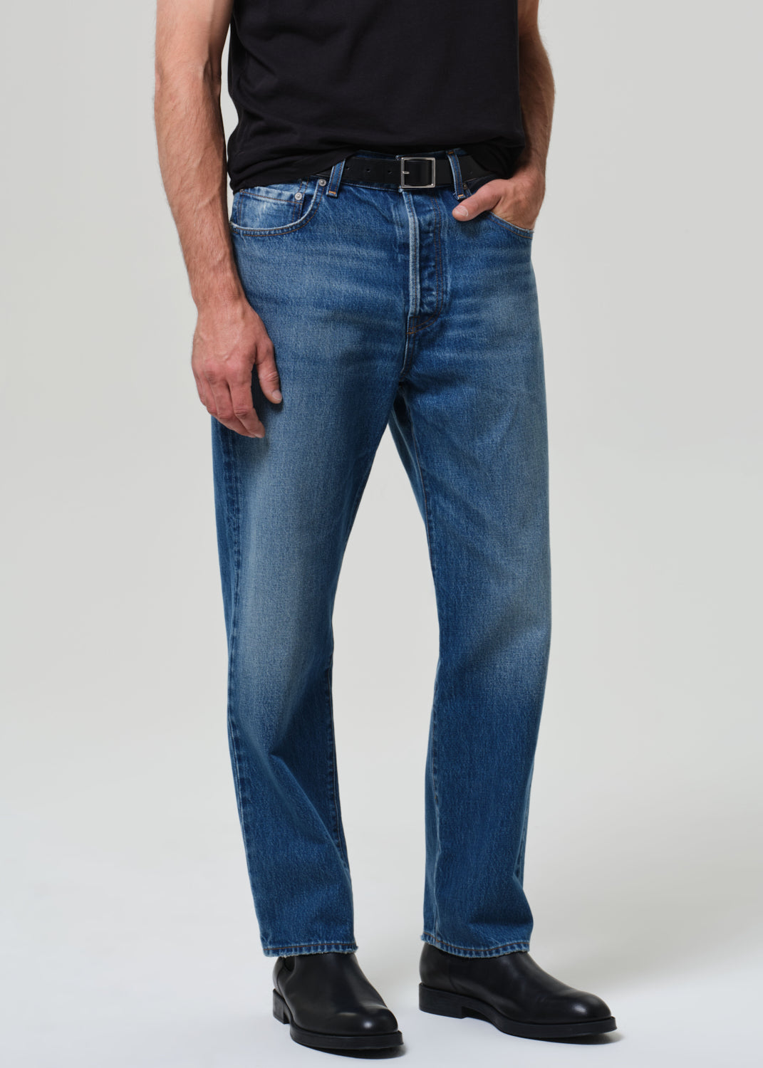 Person wearing blue jeans and black shoes on a plain background