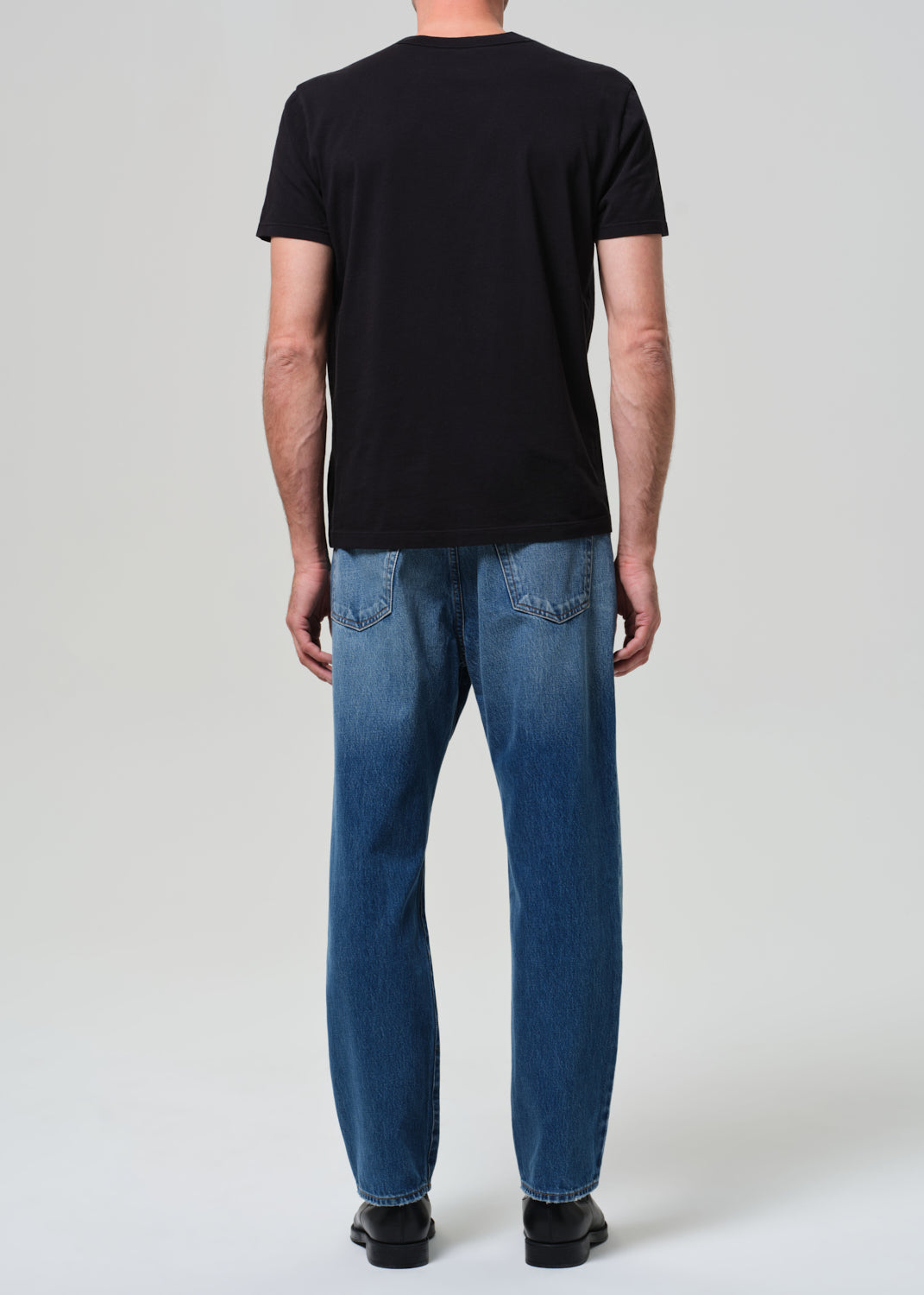Person wearing a black t-shirt and blue jeans on a white background