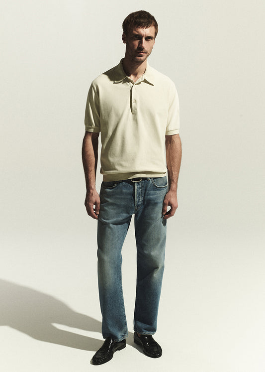 Man wearing a beige polo shirt and blue jeans against a white background