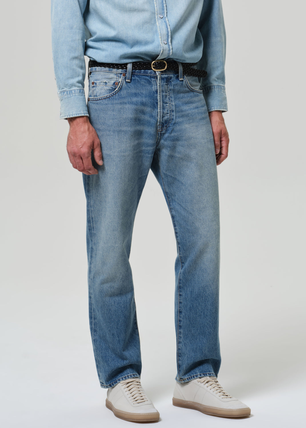 Person wearing light blue jeans and a denim shirt on a plain background