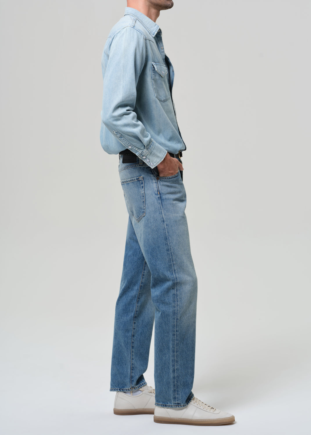 Person wearing a light blue denim shirt and jeans on a white background