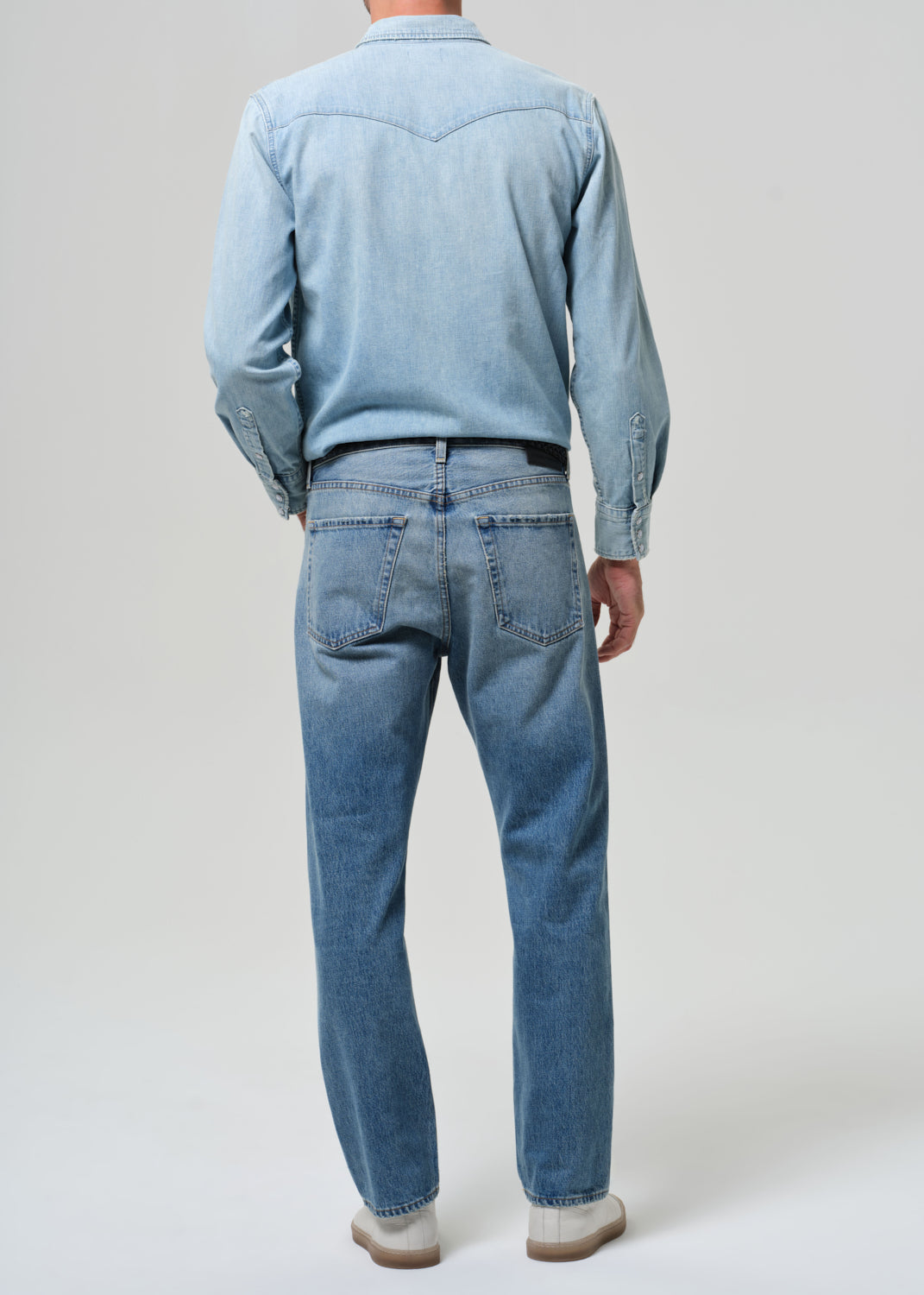 Person wearing a light blue shirt and jeans on a plain background