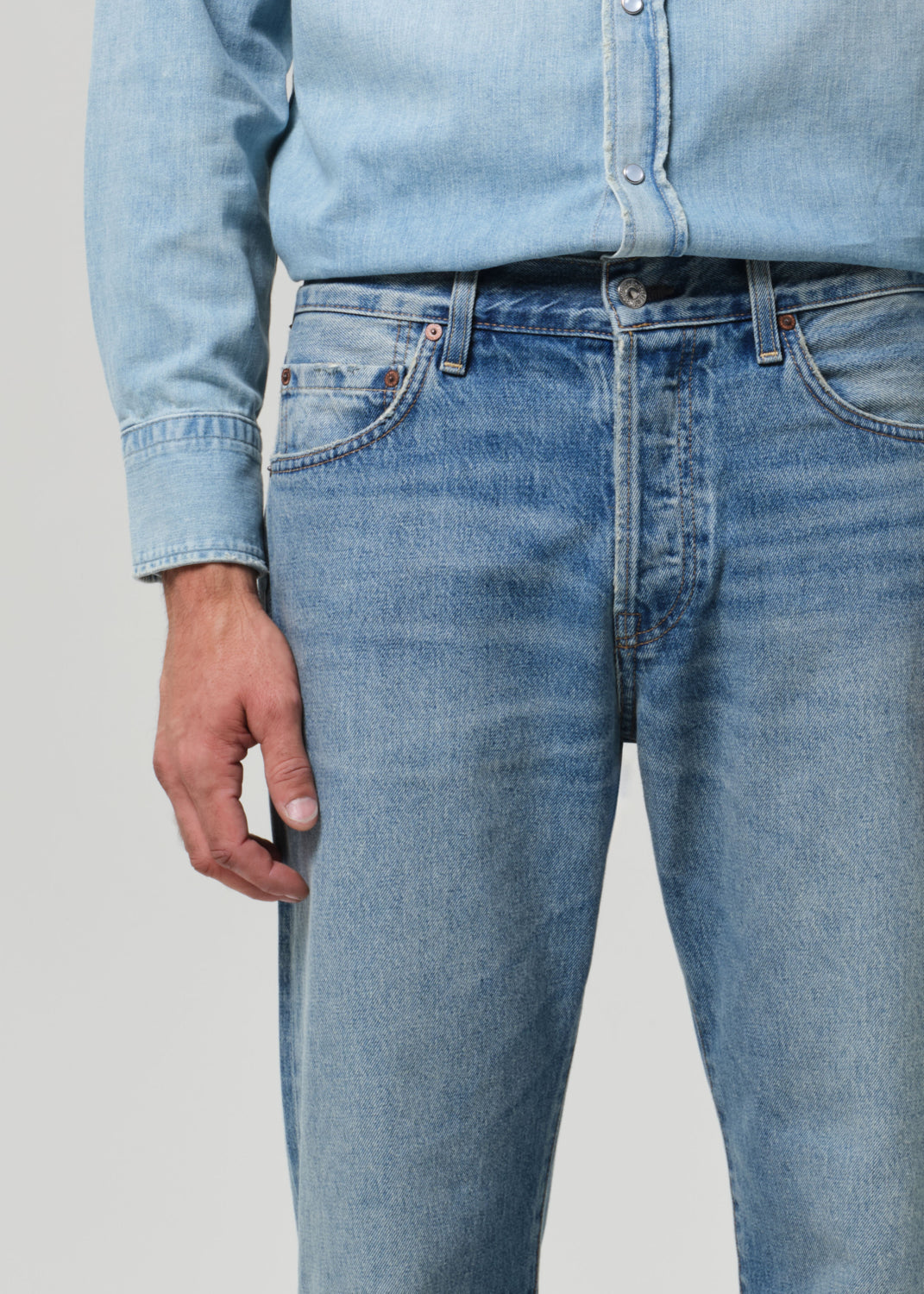 Person wearing light blue jeans and a matching denim shirt against a plain background