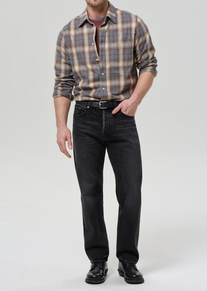 Man wearing a plaid shirt and black jeans on a grey background