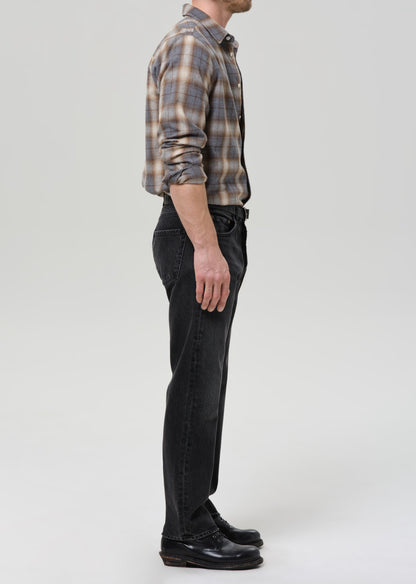 Person wearing a plaid shirt and black jeans on a grey background