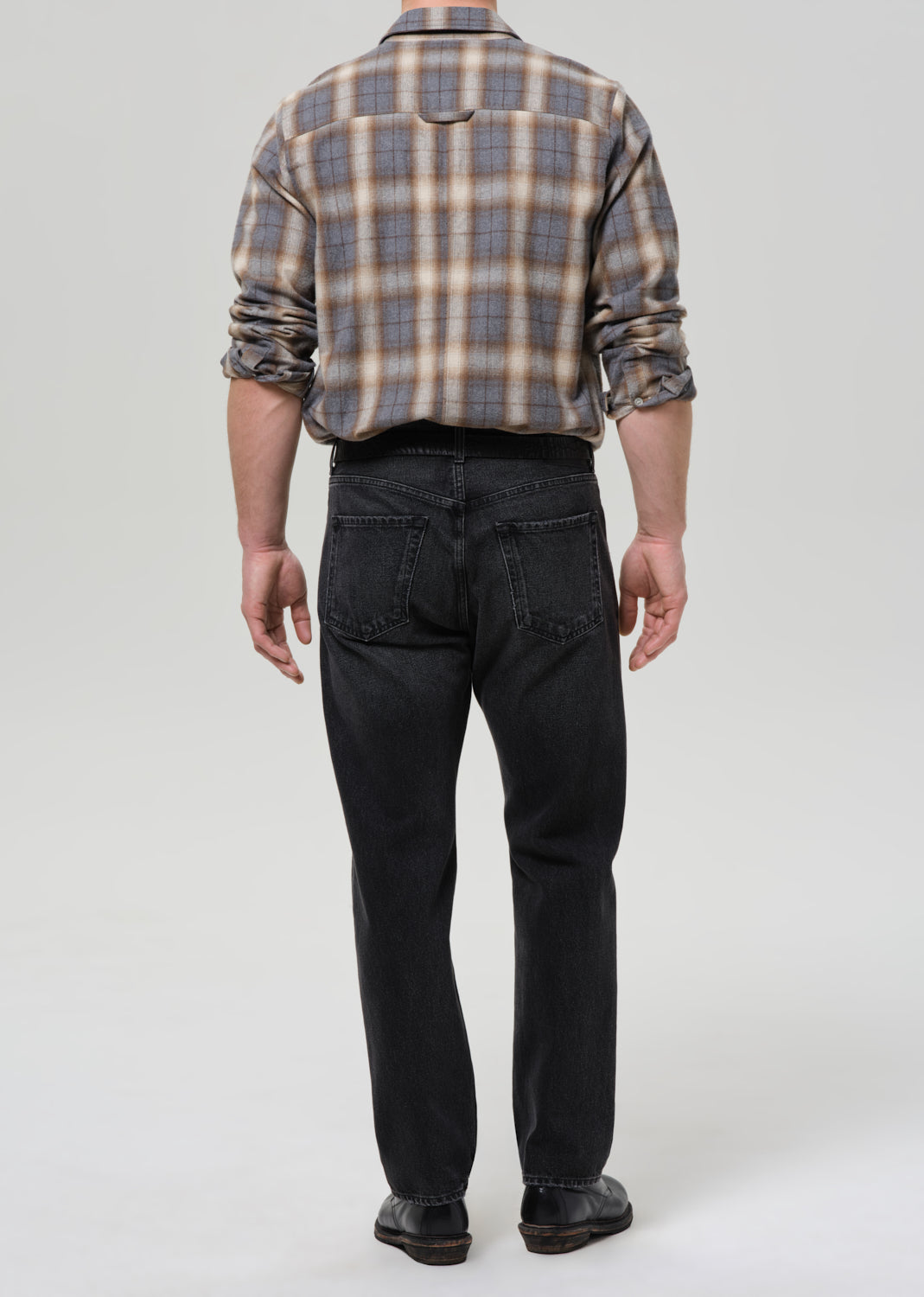 Person wearing a plaid shirt and black jeans on a grey background