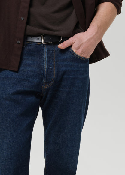 Person wearing dark blue jeans and a brown shirt on a grey background