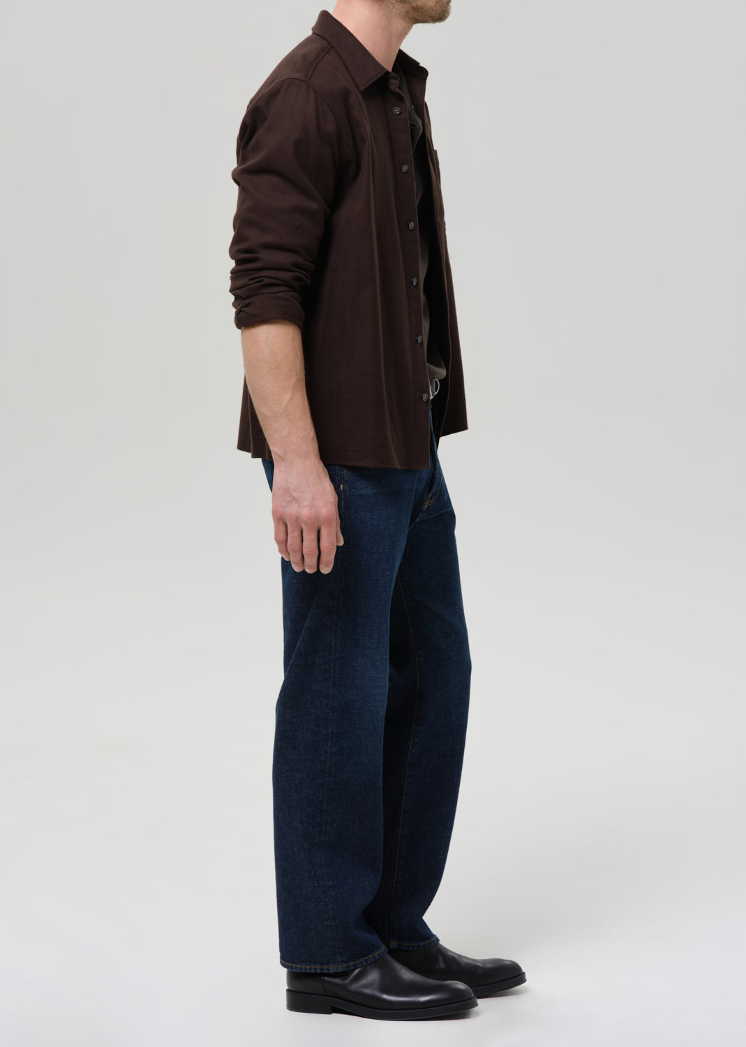 Person wearing a brown shirt and dark blue pants on a grey background