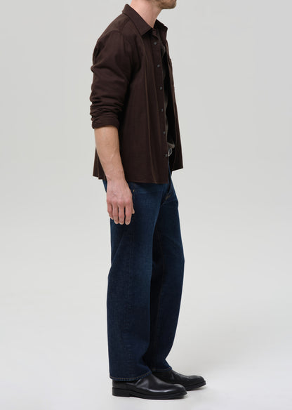 Person wearing a brown shirt and dark blue pants on a grey background