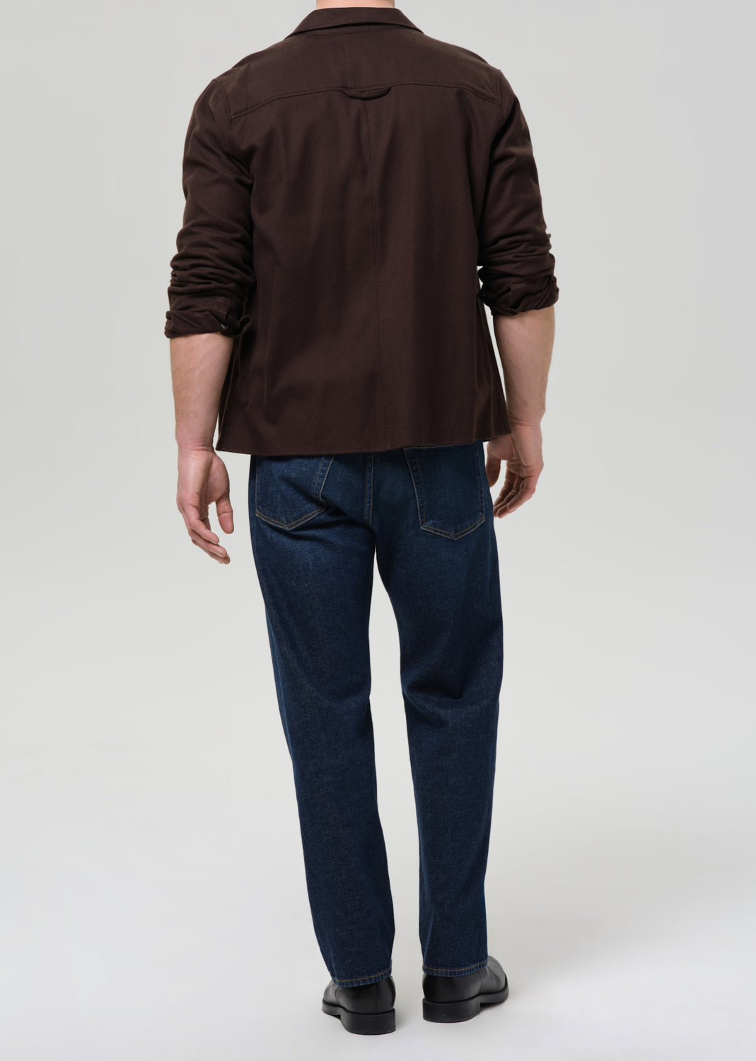Person wearing a brown shirt and dark blue jeans on a grey background