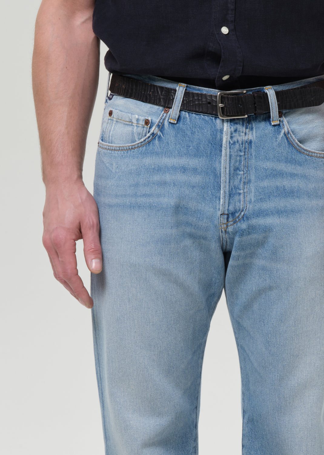 Man wearing a navy button-up shirt and light blue jeans on a plain background